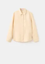 Camisa de lino color beige, de diseño recto con cuello camisero, manga larga con puños abotonados, bolsillo de parche en el pecho y cierre frontal de botones.