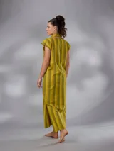 Vestido largo de lino y algodón con diseño de rayas verticales en tonos mostaza y verde. Presenta escote en V, cuello solapa ancho, mangas cortas con diseño capa, corte recto y lazo ajustable en la cintura.