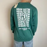 Buzo de cuello redondo color verde, con diseño gráfico estampado en la espalda con la frase 'Chase Waves' en tipografía psicodélica y texto inferior alusivo a Santa Barbara California.