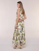 Vestido maxi sin mangas de base blanca con estampado de hojas tropicales en tonos verde y marrón. Presenta escote en V cruzado, cintura elastizada con paneles fruncidos y falda larga fluida con volados en el ruedo.