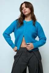 Cardigan corto de punto color rojo, con cierre frontal y cuello redondo. Presenta una textura acanalada y mangas largas.