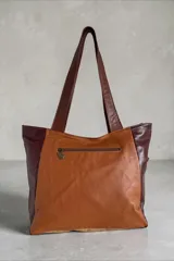 Cartera de cuero marrón estilo tote bag, con diseño en patchwork y bolsillo frontal de pelo con estampado animal print tipo vaca. Cuenta con doble asa de hombro y detalles metálicos.