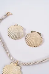 Set compuesto por un collar de cordón trenzado negro con dije central en forma de concha dorada y un par de aros a juego con diseño de concha dorada.