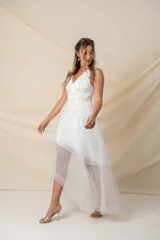 Vestido corto de tul color marfil con diseño asimétrico tipo high-low, escote en V y sin mangas. Presenta delicadas incrustaciones de flores y hojas bordadas en hilo de seda en la parte superior.
