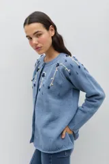 Saco de punto color azul, con cuello redondo, cierre frontal con botones forrados en crochet y mangas largas. Presenta un delicado bordado floral artesanal en la zona de los hombros y el pecho.