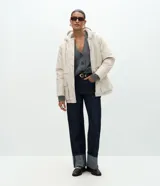 Campera parka de Marfinno confeccionada en PU con textura gomosa, color beige. Cuenta con capucha, forro interior de peluche sintético, cierre frontal con solapa y botones a presión, y bolsillos delanteros grandes con solapa.