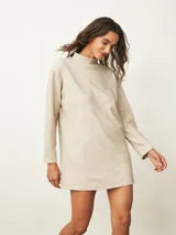Vestido corto de color beige con cuello alto y mangas largas, de corte recto y holgado.