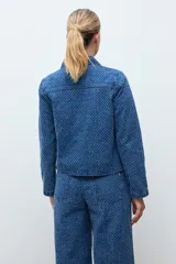 Chaqueta de jean azul con textura de efecto desgastado, cuello clásico y cierre frontal.