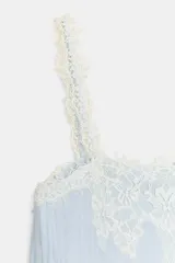 Top de estilo lencero color celeste, con escote recto y tirantes finos decorados con puntilla de encaje blanco. Presenta un detalle de encaje floral en el pecho.