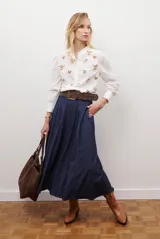 Camisa blanca con cuello mao y botones frontales, mangas largas abullonadas con puños anchos y bordados florales en tonos marrones.