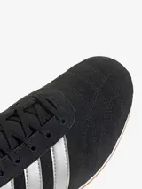 Zapatillas Adidas Taekwondo Lace negras de gamuza con las tres rayas plateadas y refuerzo plateado en el talón.