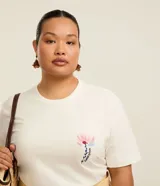 Remera de algodón color blanco, de corte holgado y alargado, con cuello redondo, manga corta y un delicado estampado floral con la frase "Flowers Bloom" en el lado izquierdo del pecho.