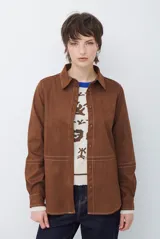 Camisa de estilo casual confeccionada en material tipo gamuza color marrón, con cuello clásico, cierre frontal con botones y costuras a la vista en tono contrastante.