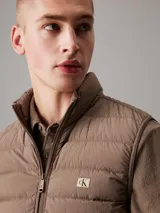 Chaleco acolchado marrón claro con cierre frontal con cremallera, cuello alto y bolsillos laterales.