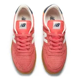 Championes New Balance T500, color rosado con la tradicional 'N' en blanco, detalles en azul marino en el talón y suela de goma color caramelo. Confeccionados en gamuza y nobuk, con puntera perforada.