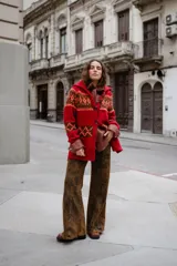 Saco tejido a mano con diseño jacquard en tonos rojo, naranja y marrón. Presenta cuello tipo polo, cierre frontal con botones grandes, mangas largas y tajos laterales en el ruedo.