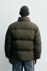 Cazadora acolchada de corte relajado confeccionada en tejido técnico color verde militar. Presenta cuello subido, cierre frontal con cremallera, mangas largas con puños elásticos y bolsillos frontales con cremallera oculta.