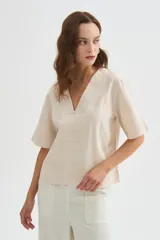 Blusa de viscosa color beige con cuello en V, mangas cortas amplias y detalles de pespuntes decorativos en el frente y las mangas.