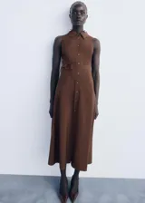 Vestido midi de corte evasé en color marrón, con cuello camisero, sin mangas y cierre frontal con botones. Incluye un cinturón ajustable a tono con hebilla.