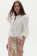 Camisa blanca de algodón, de corte clásico y atemporal, con cuello mao, mangas abullonadas y detalle de volados en la botonera frontal oculta.