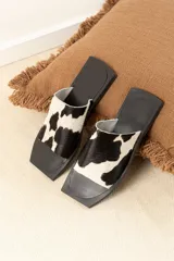 Sandalias planas con punta cuadrada, base negra y capellada de cuero marrón con textura trenzada.