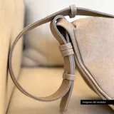 Bandolera de cuero color beige con correa ajustable y cierre superior con cremallera.