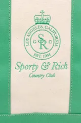 Bolso tote de lona color crema con base y asas en verde. Estampado frontal con el logo de la marca Sporty & Rich.