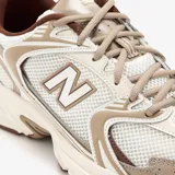 Championes New Balance modelo 530, color beige y blanco con detalles en marrón, confeccionados en malla transpirable y superposiciones de cuero sintético. Cuentan con entresuela con tecnología ABZORB y el característico logo "N" en los laterales.