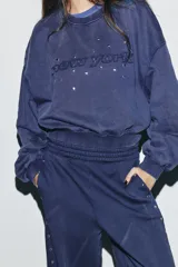 Sudadera de cuello redondo y manga larga con efecto lavado. Presenta texto bordado en el frente y aplicación de tachas decorativas. Posee puños y ruedo con acabado en rib.