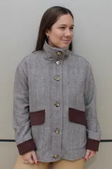 Campera de paño de lana en color beige jaspeado, con diseño oversize. Presenta detalles en pana color marrón chocolate en los puños y en las tapas de los bolsillos frontales. Cuenta con cierre frontal de botones grandes y cuello alto.