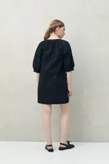 Vestido corto negro con bordado floral blanco, escote redondo con abotonadura frontal y mangas 3/4 abullonadas con pliegues en los hombros.