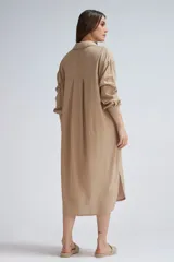 Camisa larga de lino color beige, de corte oversize, con mangas largas, cuello camisero y cierre frontal de botones. Presenta dobladillo curvo con aberturas laterales.