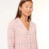 Conjunto de pijama largo de dos piezas, compuesto por camisa de manga larga con cuello y pantalón largo, ambos con estampado a cuadros en tonos rosa y blanco.