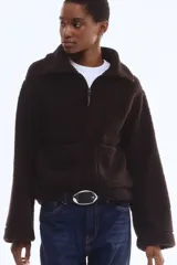 Campera de sherpa color marrón oscuro, con cuello elevado, cierre frontal y bolsillos de parche en los laterales.