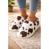 Pantuflas de estar por casa con diseño de manchas de vaca, confeccionadas en material afelpado suave. Presentan un diseño sin talón y suela de PVC antideslizante.