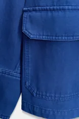 Chaqueta azul de corte recto, con cuello camisero, manga larga y cierre frontal de botones metálicos. Cuenta con un bolsillo de parche en el pecho y dos bolsillos con solapa en la parte inferior delantera.