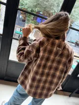 Campera reversible de corte holgado con cuello alto. De un lado presenta un diseño a cuadros en tonos marrones y beige, y del otro lado un diseño liso. Cuenta con cierre frontal de botones y mangas largas.