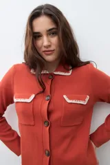 Chaqueta tejida de punto color naranja, con cuello camisero, cierre frontal de botones y dos bolsillos frontales con solapa. Presenta detalles de bordado en contraste en el cuello y los bolsillos.