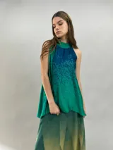 Blusa de satén con escote halter y cuello elevado anudado lateralmente. Presenta un diseño estampado degradado en tonos verde esmeralda y azul, con corte holgado y caída fluida.