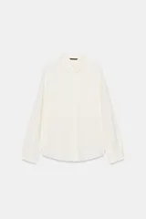 Camisa de color blanco con cuello de solapa, manga larga con pliegues, bajo asimétrico y cierre frontal con botones forrados.