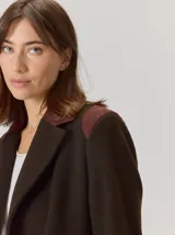 Tapado de lana color marrón oscuro, con diseño de corte recto a la rodilla, solapas clásicas y cierre frontal con botones. Presenta detalles en contraste en los hombros y laterales.