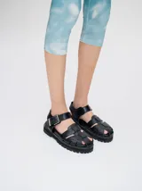 Sandalias romanas de cuero tostado, estilo chunky con plataforma y suela tractora de goma negra. Cuentan con tiras cruzadas en el empeine y tira ajustable con hebilla metálica en el tobillo.