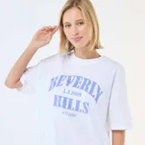 Camiseta de corte oversize color blanco, con cuello redondo y mangas cortas. Presenta un estampado frontal con la inscripción 'Beverly Hills L.A. 1989 West Co' en tonos azules.
