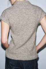 Top de punto color beige, con cuello subido, manga corta y detalle de tejido efecto cepillado.