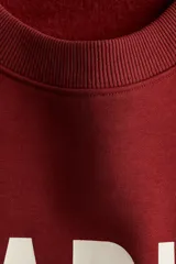 Buzo de cuello redondo con hombros caídos y diseño estampado con texto en el frente. Presenta puños y bajo acanalados.