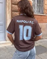 Camiseta de fútbol color marrón con cuello en V y detalles en celeste, inspirada en el Napoli F.C., con diseño de mangas cortas y sponsors impresos en el frente.