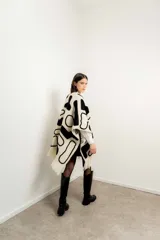 Ruana tejida en lana con diseño de formas abstractas en color negro sobre fondo crudo, con terminación de flecos en el ruedo.