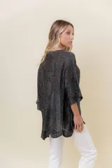 Buzo de tejido liviano con brillo sutil tipo lurex, color beige o dorado claro. Presenta un calce suelto (oversize) con mangas amplias y cuello redondo. El ruedo tiene un detalle de terminación festoneado con pequeños calados.