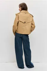 Cazadora corta de estilo gabardina en color tostado, con diseño cruzado de doble botonadura, solapas amplias, mangas largas con trabillas en los puños y hombreras.