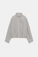 Chaqueta estilo bomber con estampado de cuadros vichy en blanco y negro, de cuello subido, manga larga y bolsillos delanteros de vivo. Cuenta con bajo abullonado y cierre frontal con cremallera oculta.
